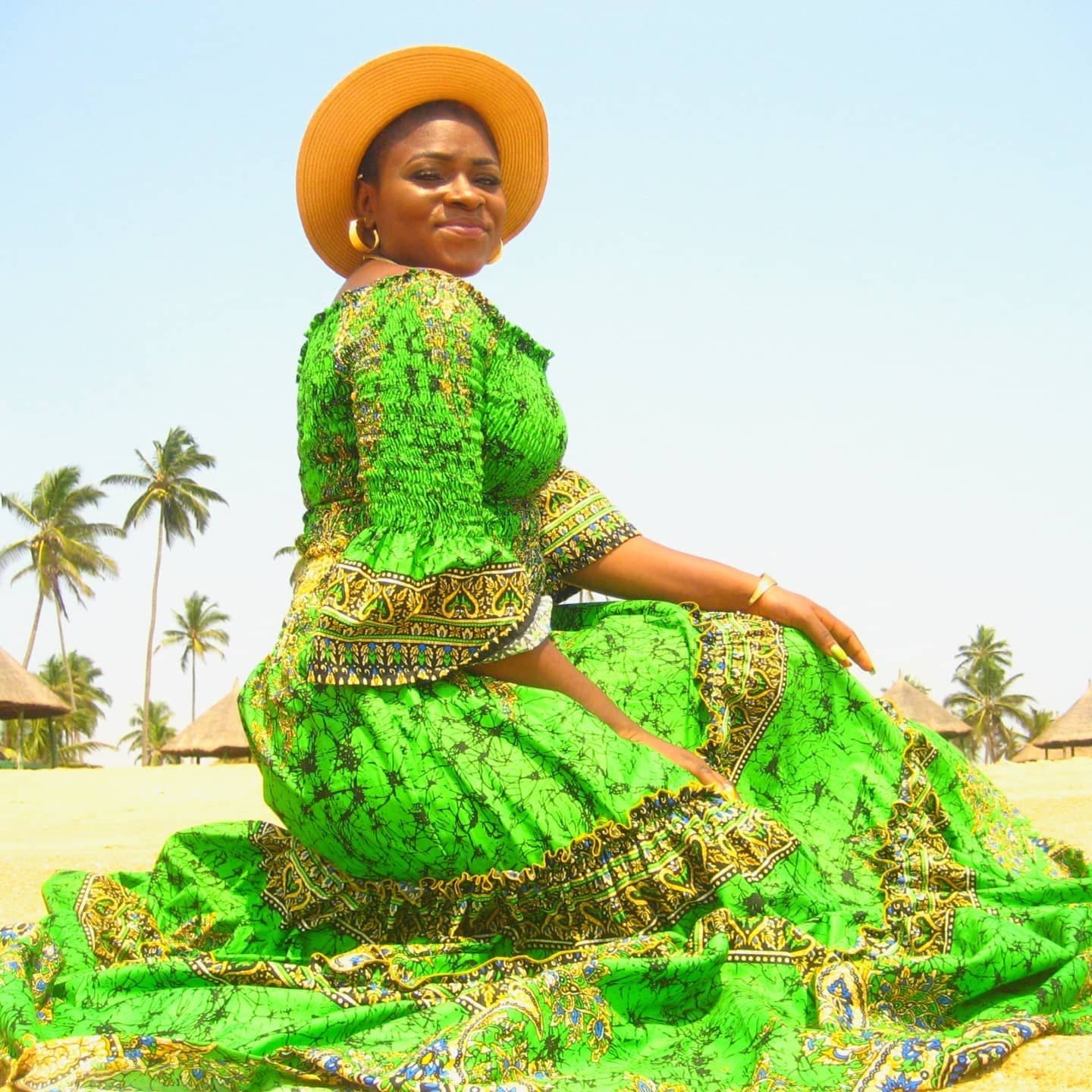 A woman in a flowing green Ankara gown on a beach