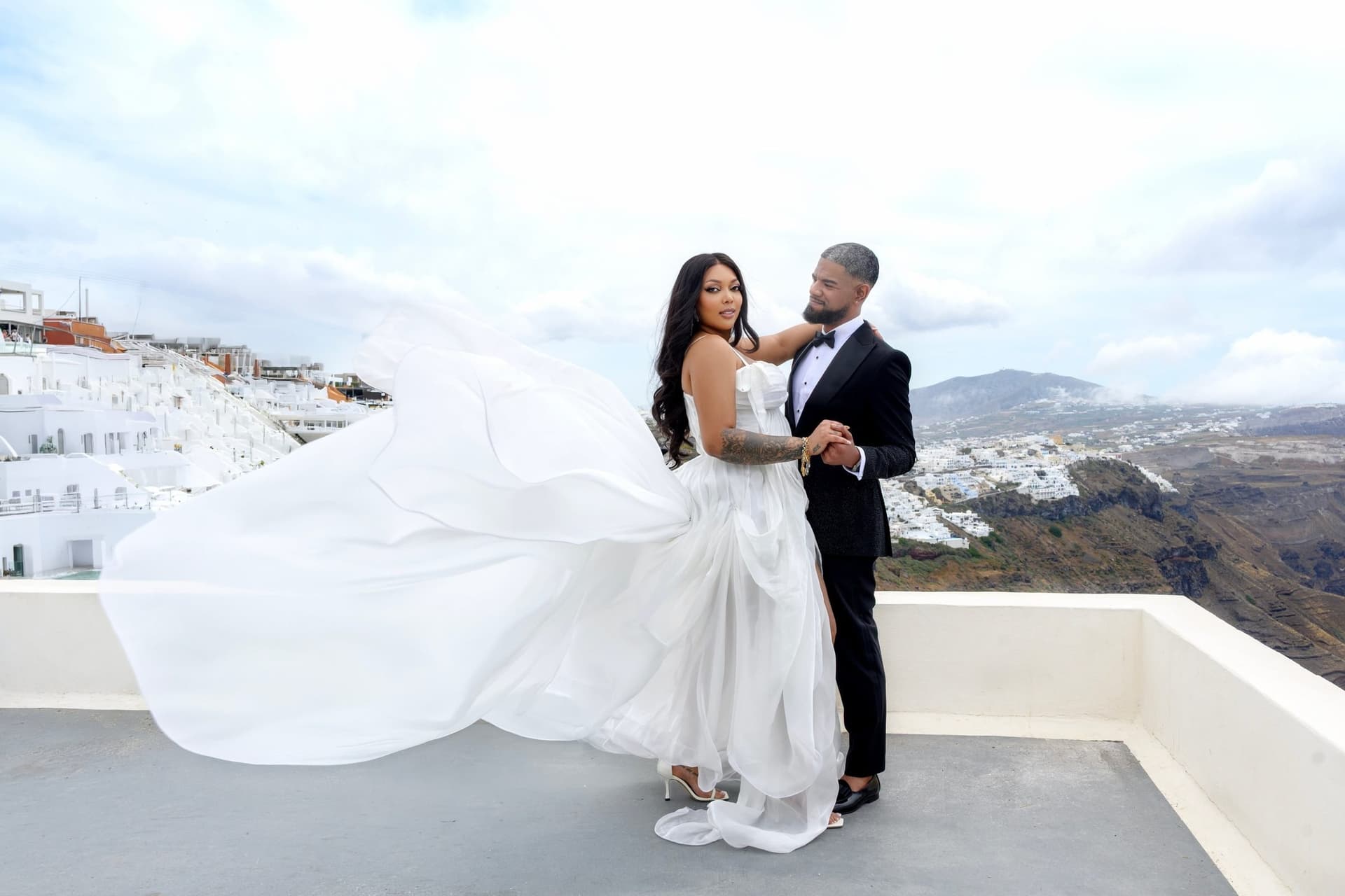 A bride in a flowing Lizkon gown with the groom on a terrace above the sea in Santorini, Greece