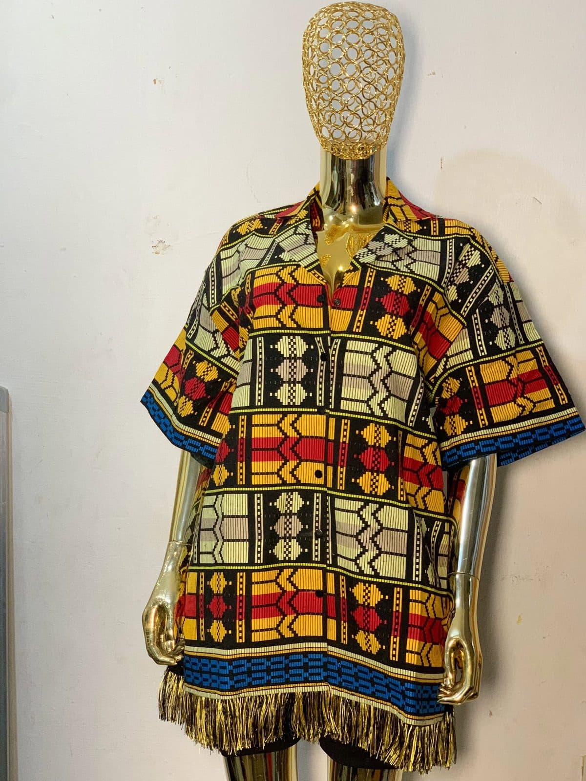 An Ankara print shirt with a gold fringe hem on a mannequin