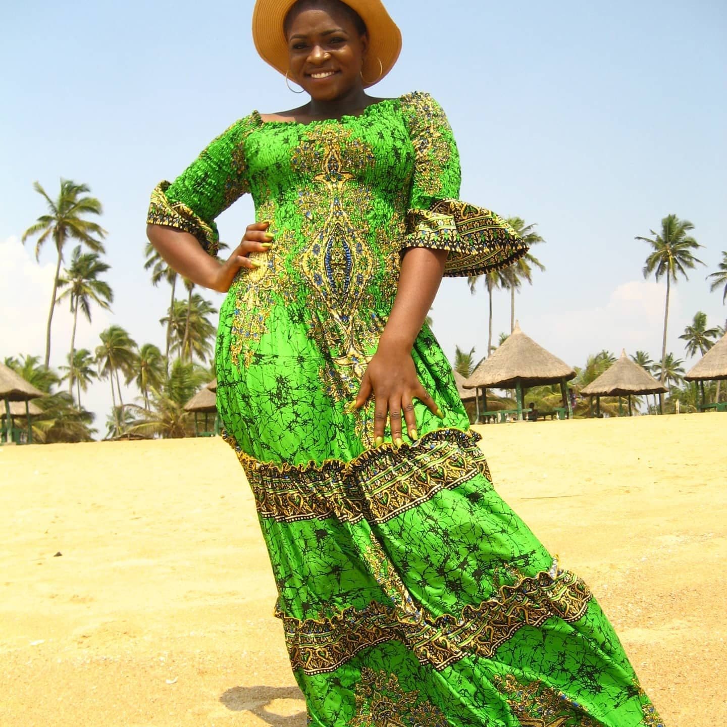 A woman in a flowing green Ankara gown on a beach