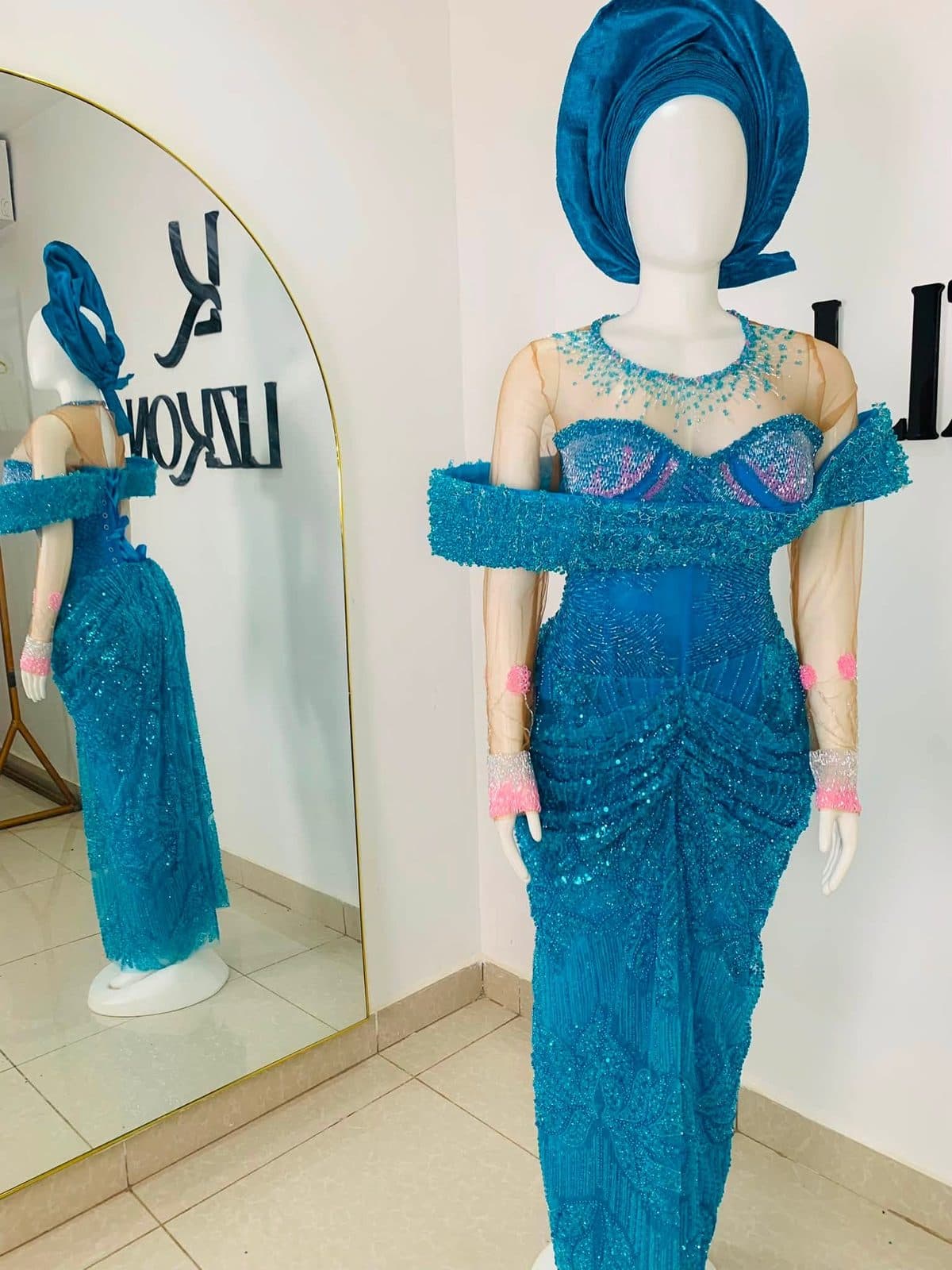 A teal gown on a dress form in front of the Lizkon wall in the Abuja studio
