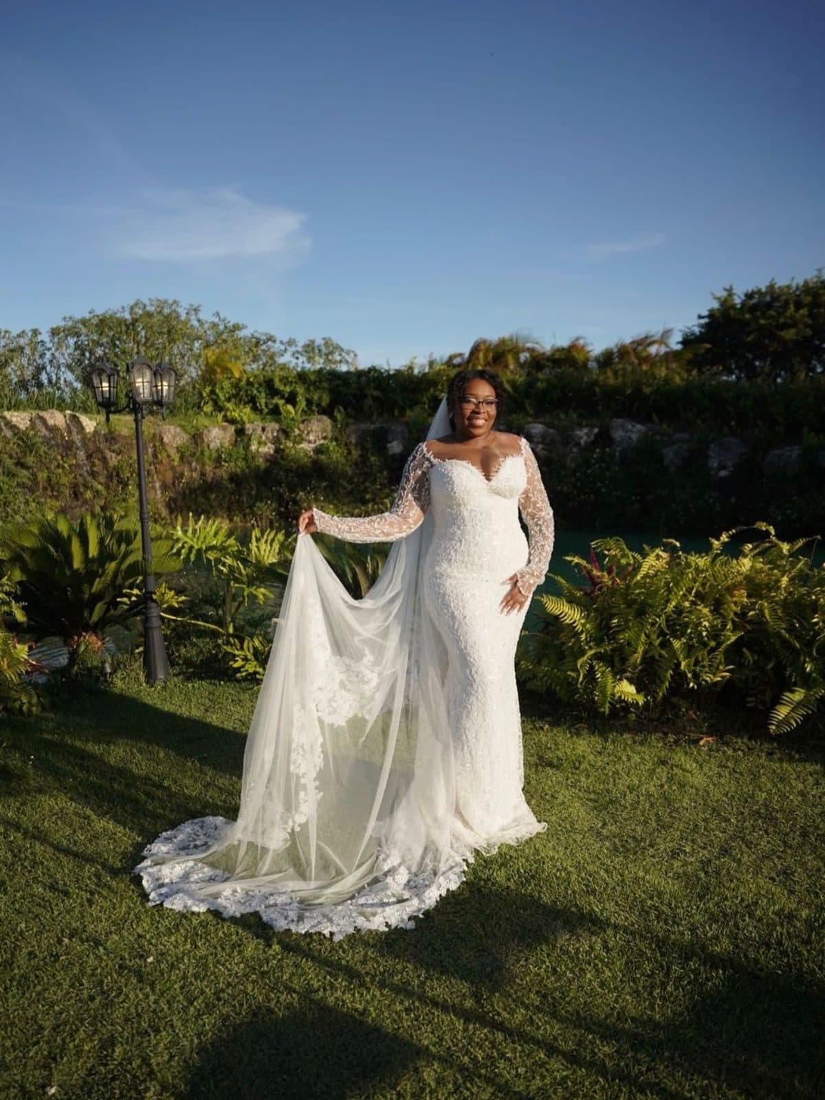 A bride in a lace mermaid gown and long veil in a garden