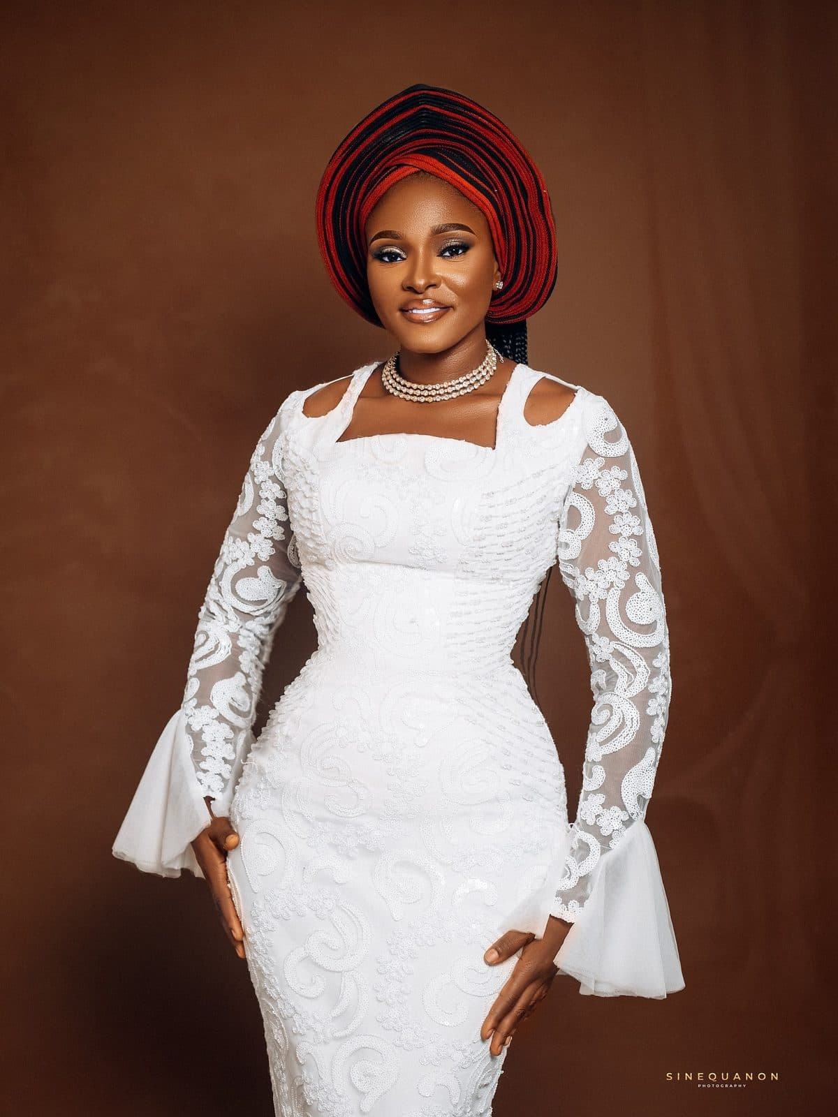 A woman in a white lace dress with flared sleeves and a gele